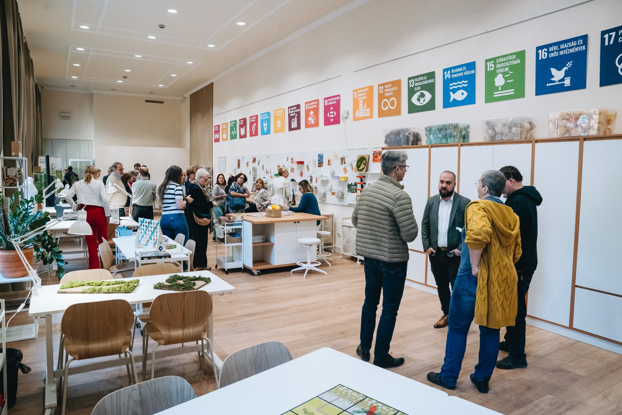 A makerspace room in the library with UN SDG posters on the walls, people chatting and working at tables with recycled materials.